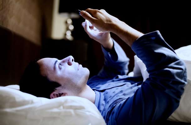 Man laying in bed looking at his phone