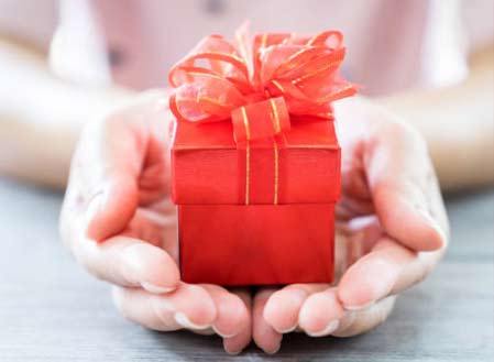 Hands holding small gift package with big red bow on top