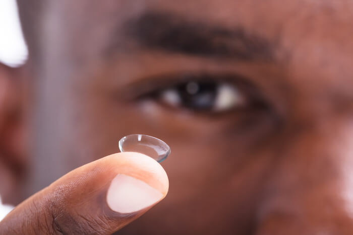 close up of contact lens on finger with face in background